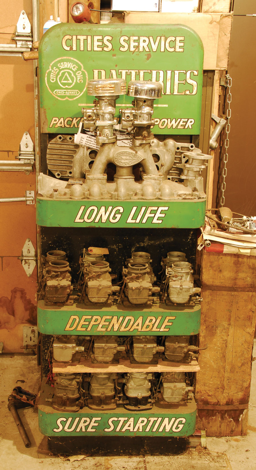 An old Cities Service Batteries rack was rescued from an old gas station and now serves as the perfect display to an old Eddie Meyer two-pot intake and a squadron of various vintage carbs