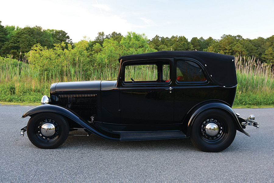black 1932 Ford B-400 body profile on road with green bushes in the background