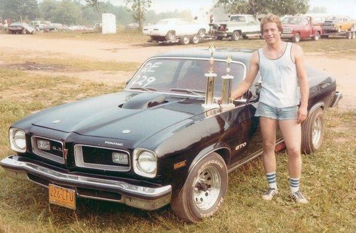 Young Rick Love photographed next to a hotrod with two trophies sitting on the hood