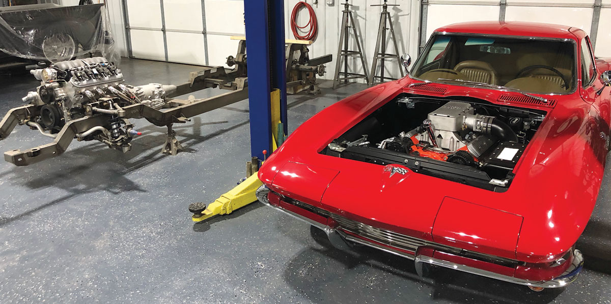 a red classic corvette sits in a garage with the hood lifted