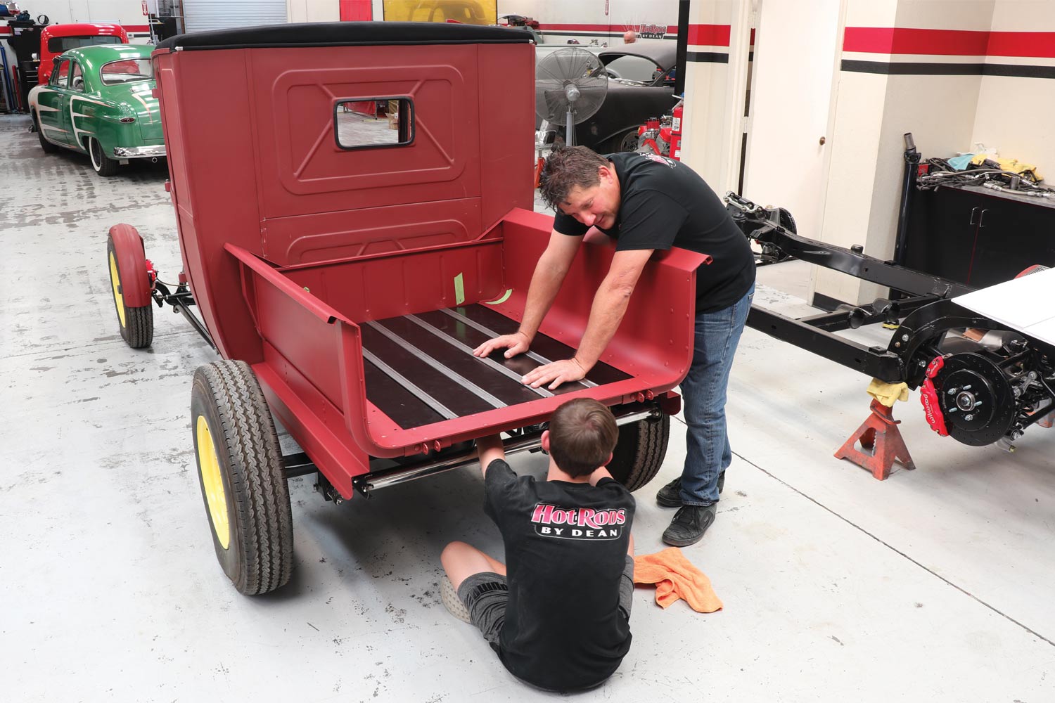 What better way to get younger hot rodders involved than to make them slide under the project and do all of the grunt work! Here Dean Livermore (standing) of Hot Rods by Dean (HRBD) is showing Zach Livermore, next generation of HRBD, the “ins and outs” of installing a BedWood® kit