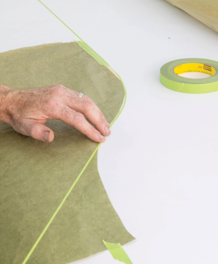 Once the shape is transferred to the masking paper then he uses 1/8-inch fineline tape to hold the paper in position. The fineline tape will serve as the edge.
