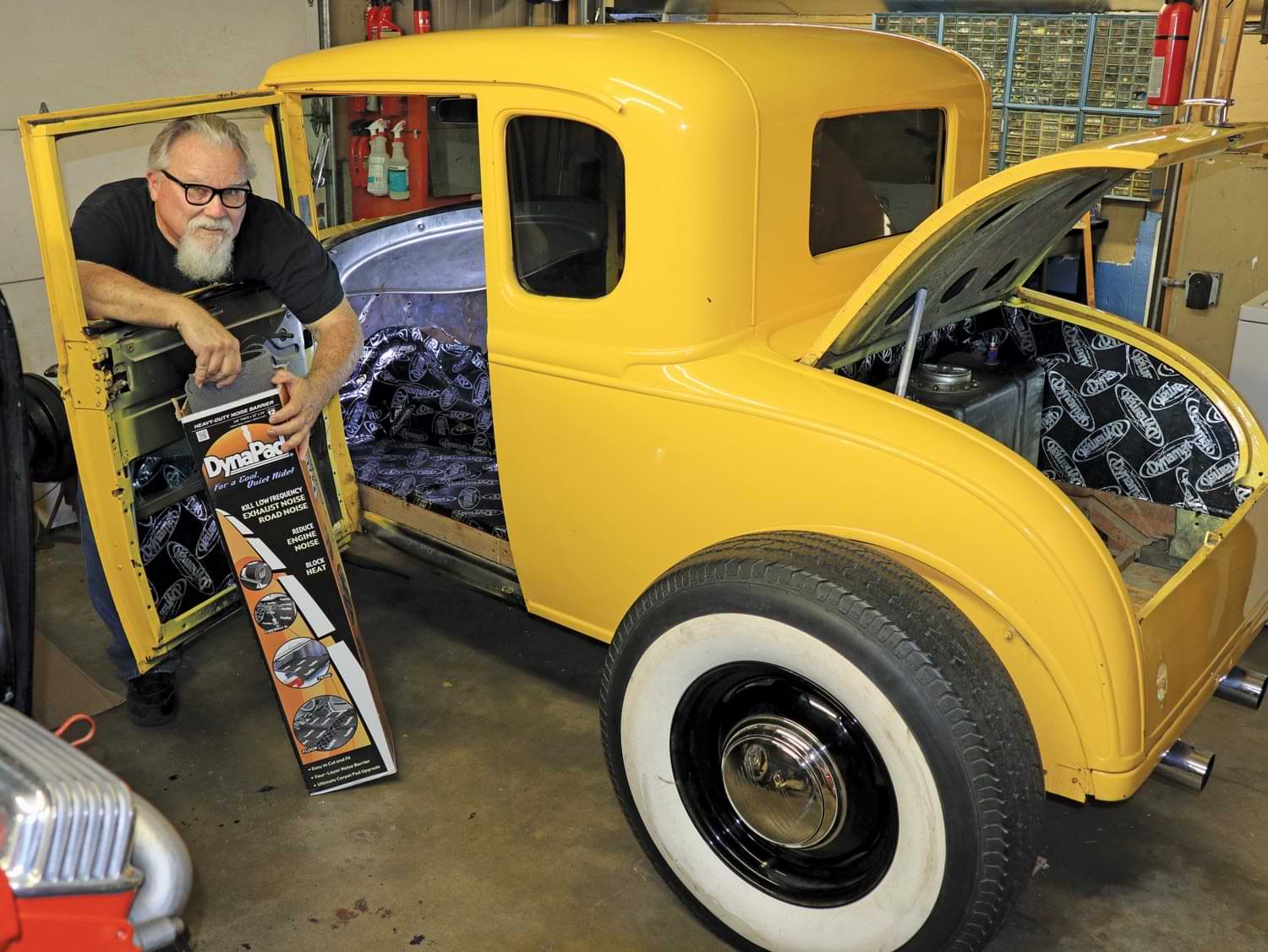mechanic stands next to a yellow Chadly Coupe holding a package of Dynaliner