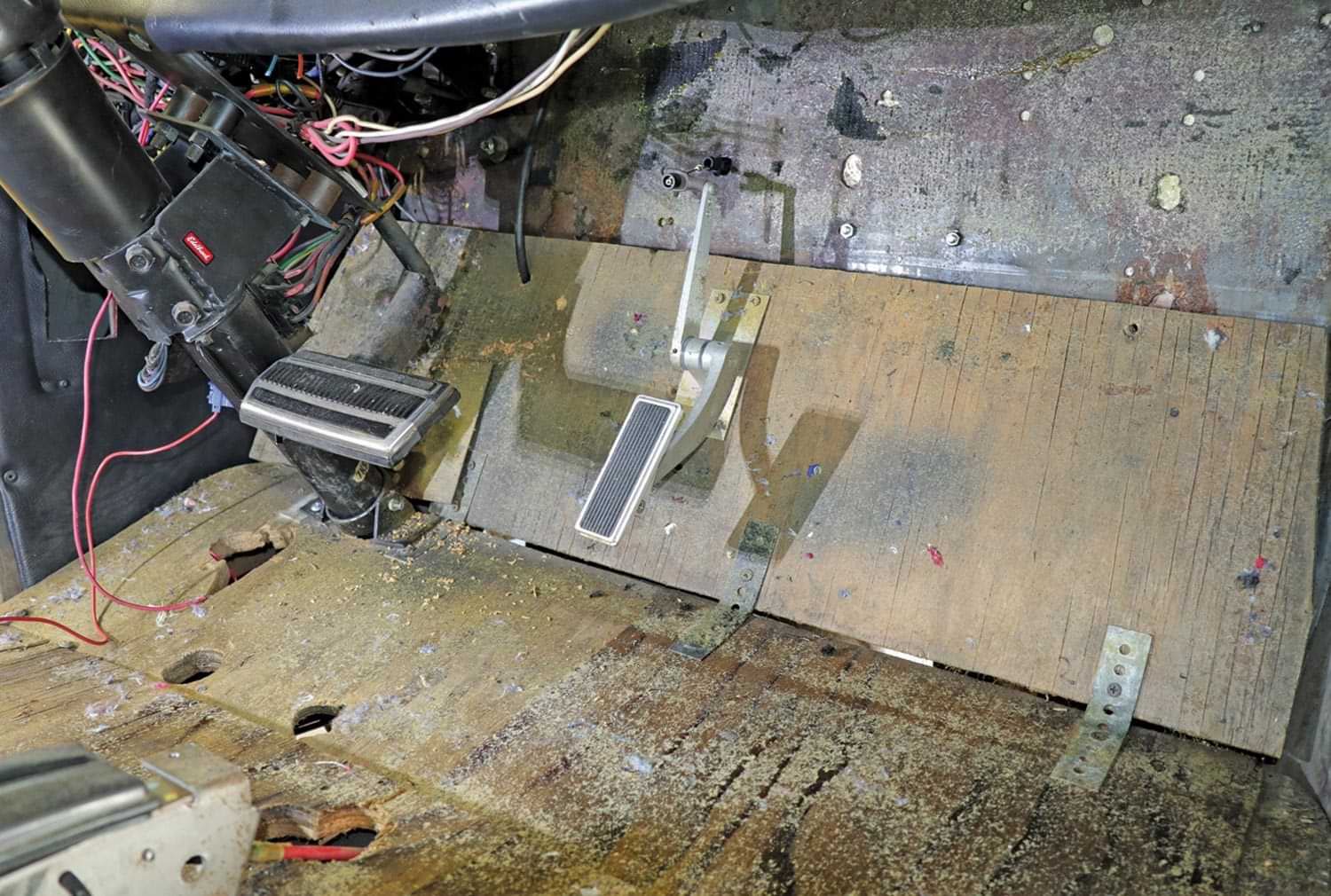 the removed carpeting reveals major problems in the floors, running from a hole-riddled plywood toeboard rearward to a water-damaged particle board trunk floor