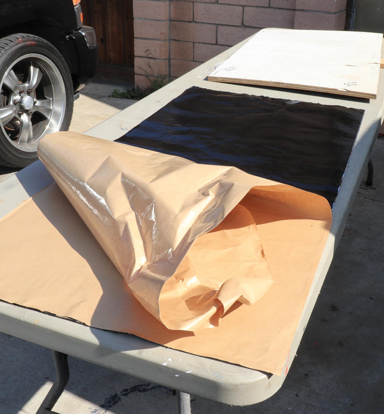 a sheet of Dynamat Xtreme sits on a table with a portion of the brown wax paper backing peeled