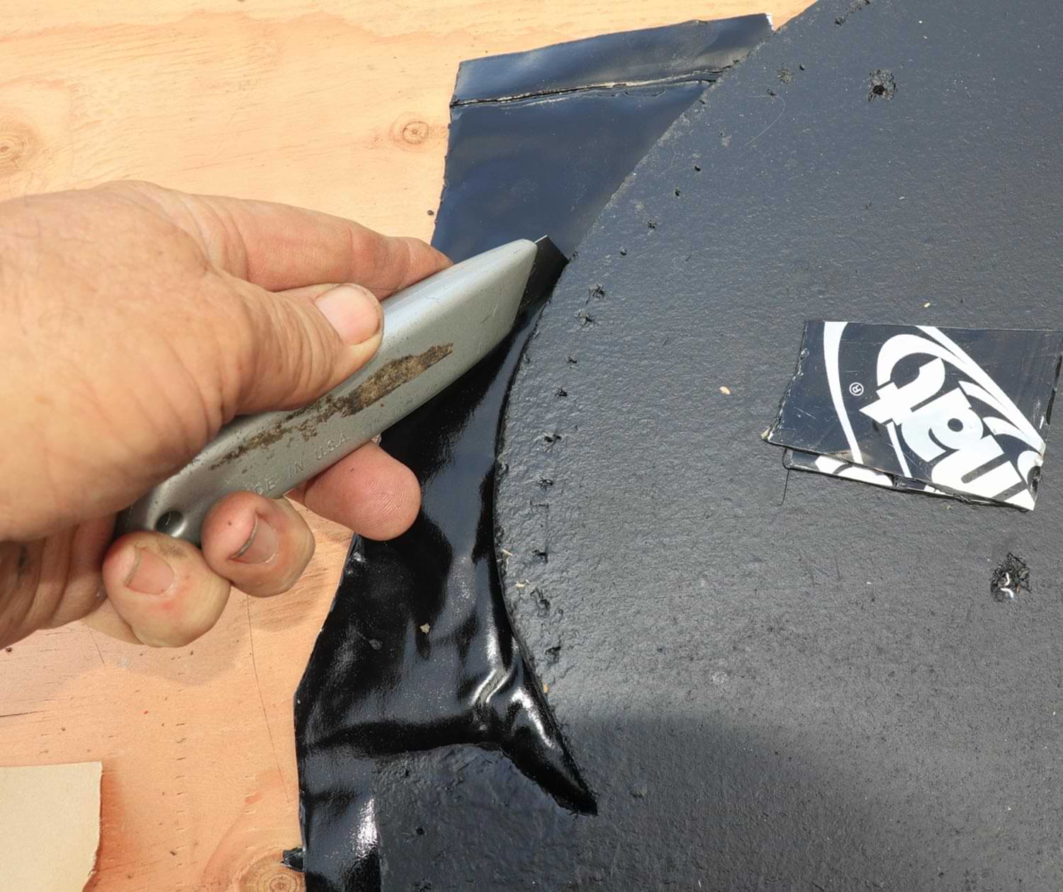 mechanic uses the matte knife to trim a Dynamat sheet around a part before placement