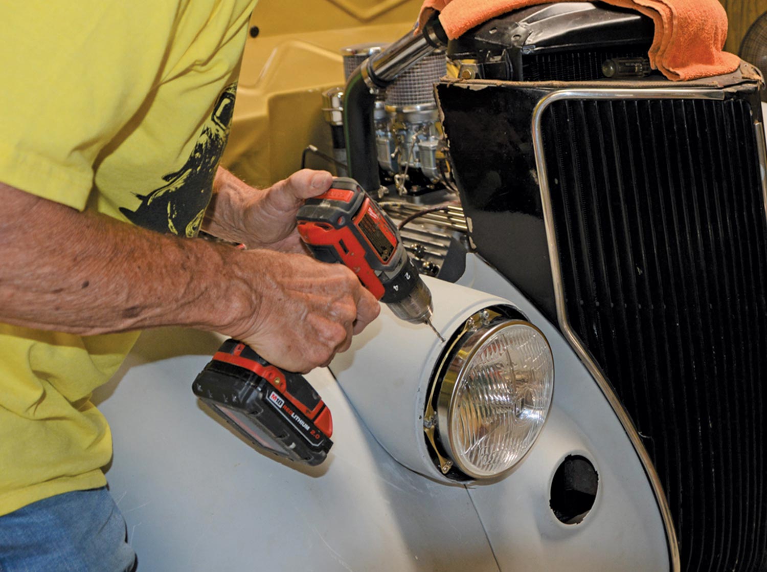 mechanic uses a drill on the reinstalled headlight