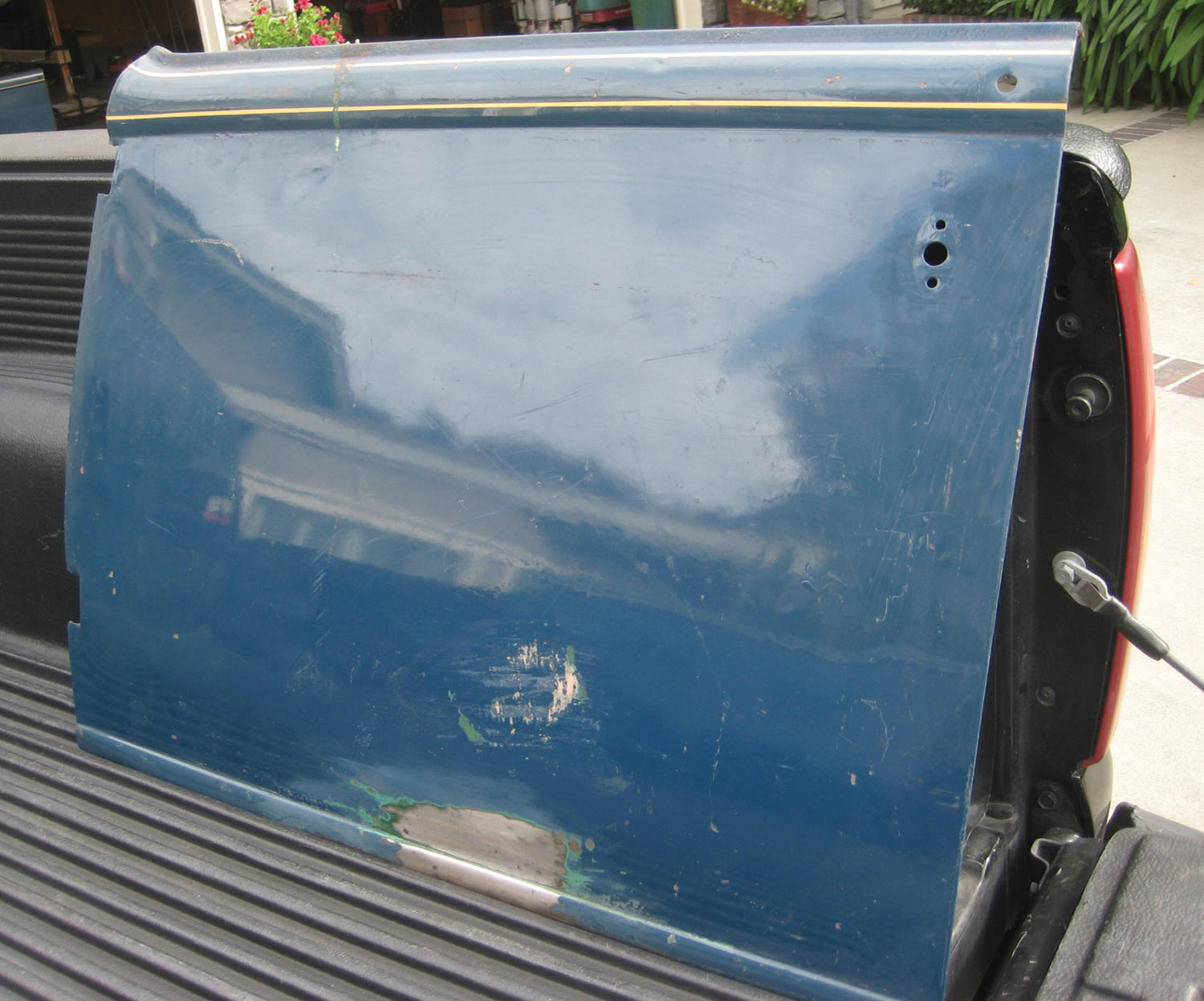a blue driver side door, showing a few bumps and scratches sits in the back of a truck