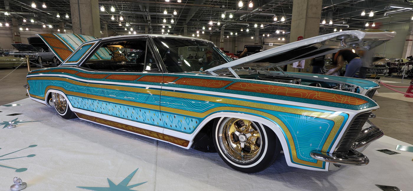 passenger side quarter view of a soft turquiose ’65 Buick Rivi lowrider with unique patterned paint work