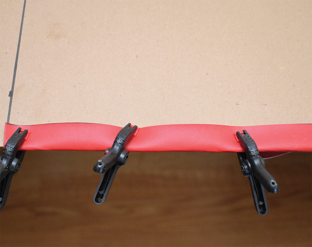 Material stretched over panel edge, glued and clamped