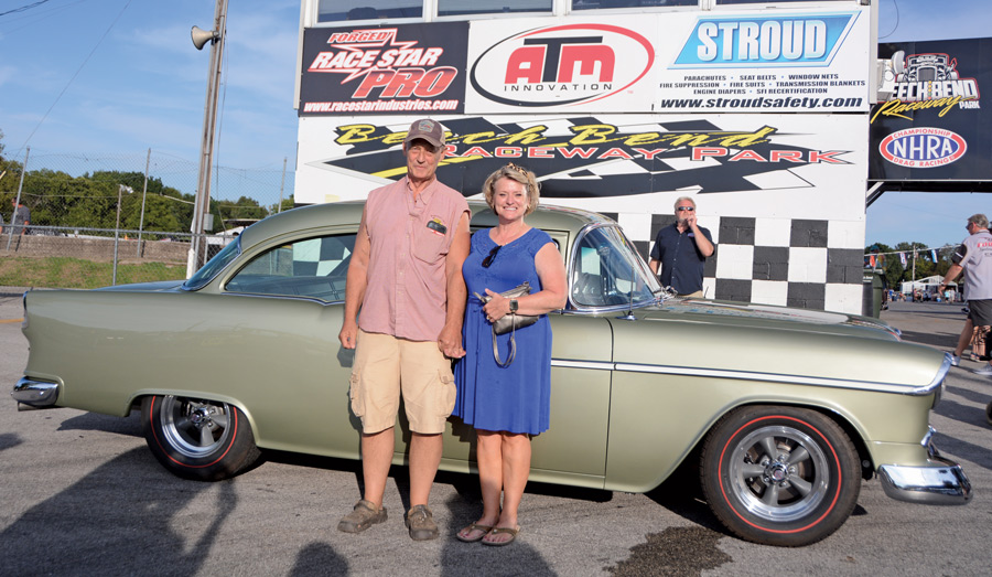 couple standing in front of their light green '55 Chevy