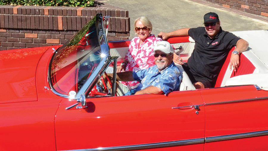 3 people sitting in an open-top bright red convertible