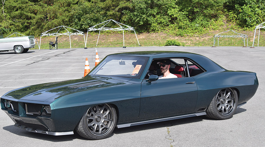 A dark grey ’69 Firebird on asphault with greenery in the background
