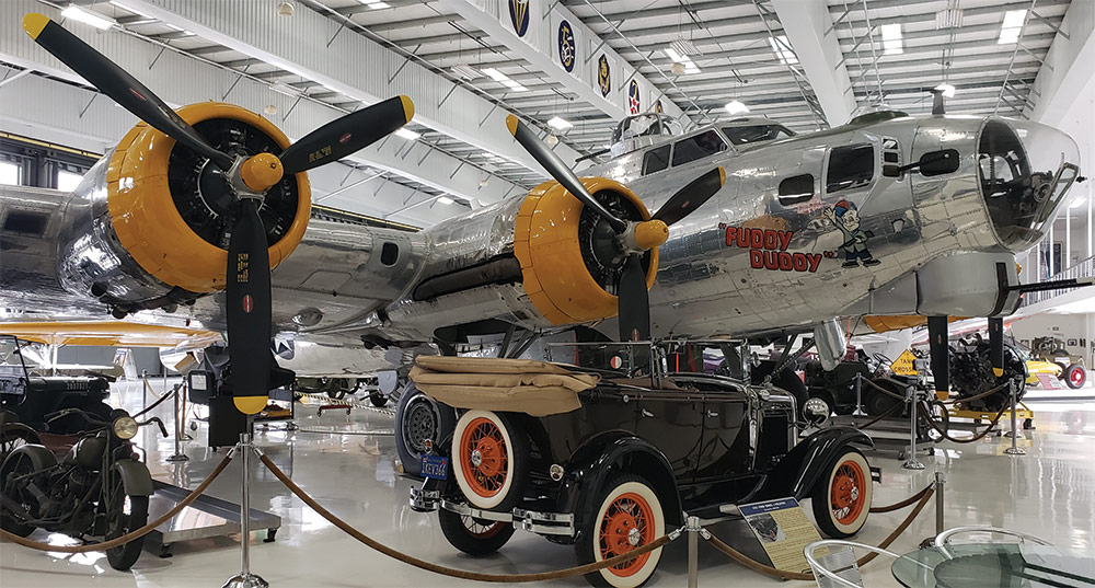 Black '31 Ford Phaeton with orange wheels and whitewalls next to "Fuddy Duddy" B-17
