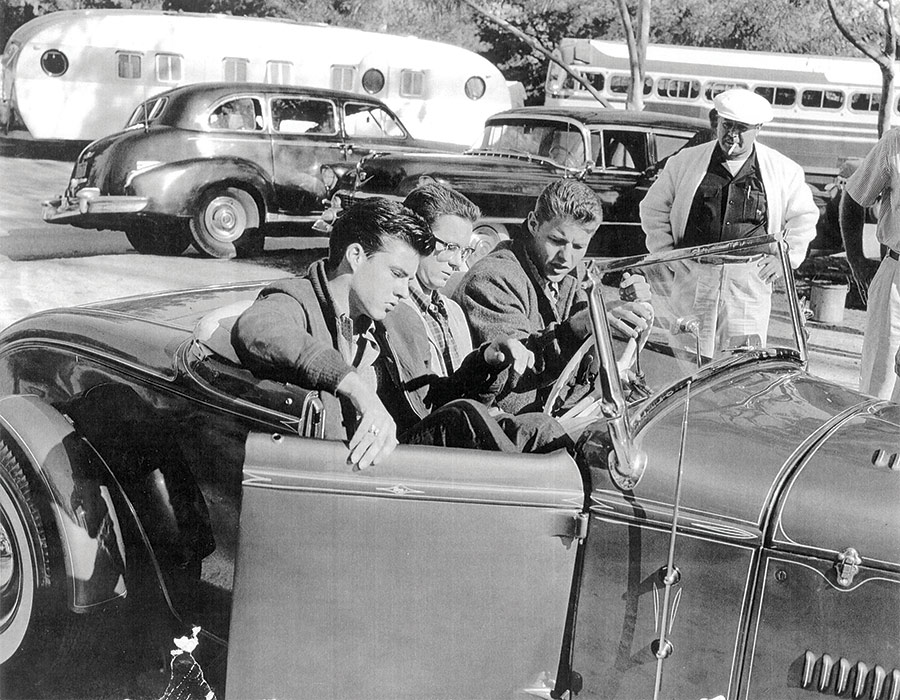 Tony La Mesa behind a roadster watching three young men get in a two seater vehicle