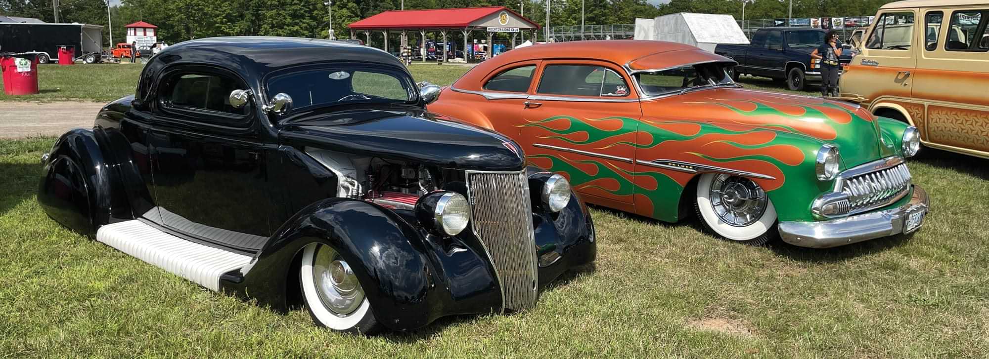two cars, a black classic coupe and a classic chevy DeLuxe with orange and green flame paint, parked at the Jalopy Jam Up