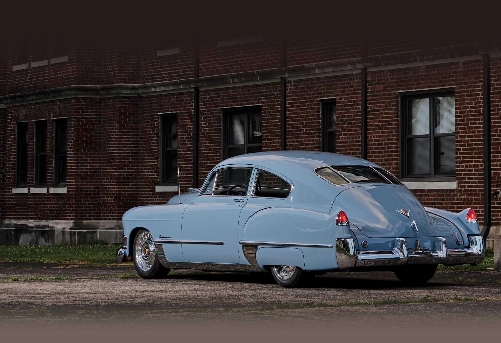 three quarter driver's side rear view of the pale blue ’49 Cadillac Series 62 Sedanette parked near a red brick building