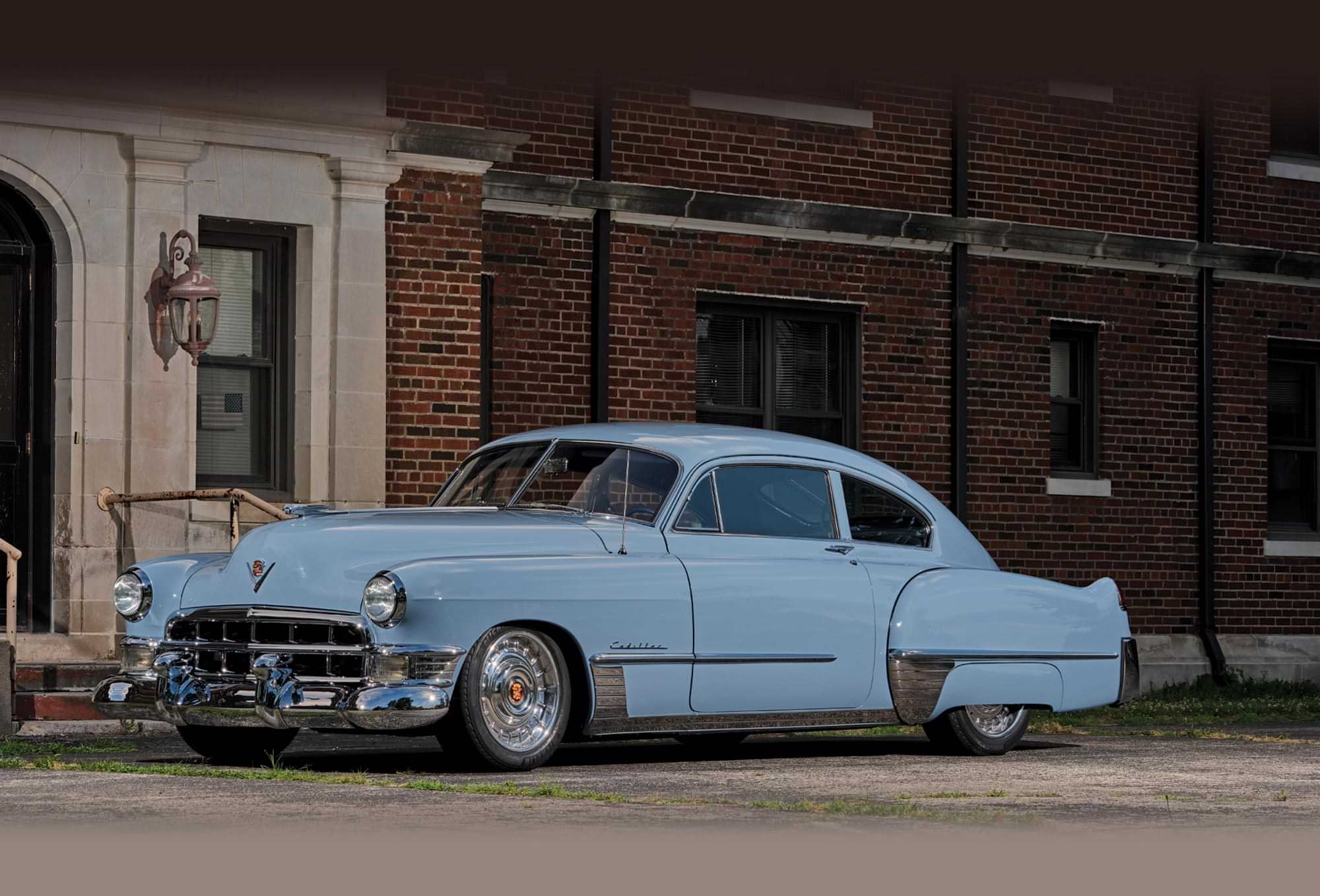 three quarter driver's side front view of the pale blue ’49 Cadillac Series 62 Sedanette parked in front of a red brick building