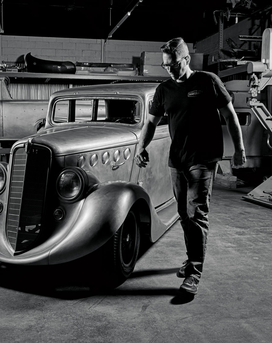 man standing next to a '36 Willys Sedan in a garage