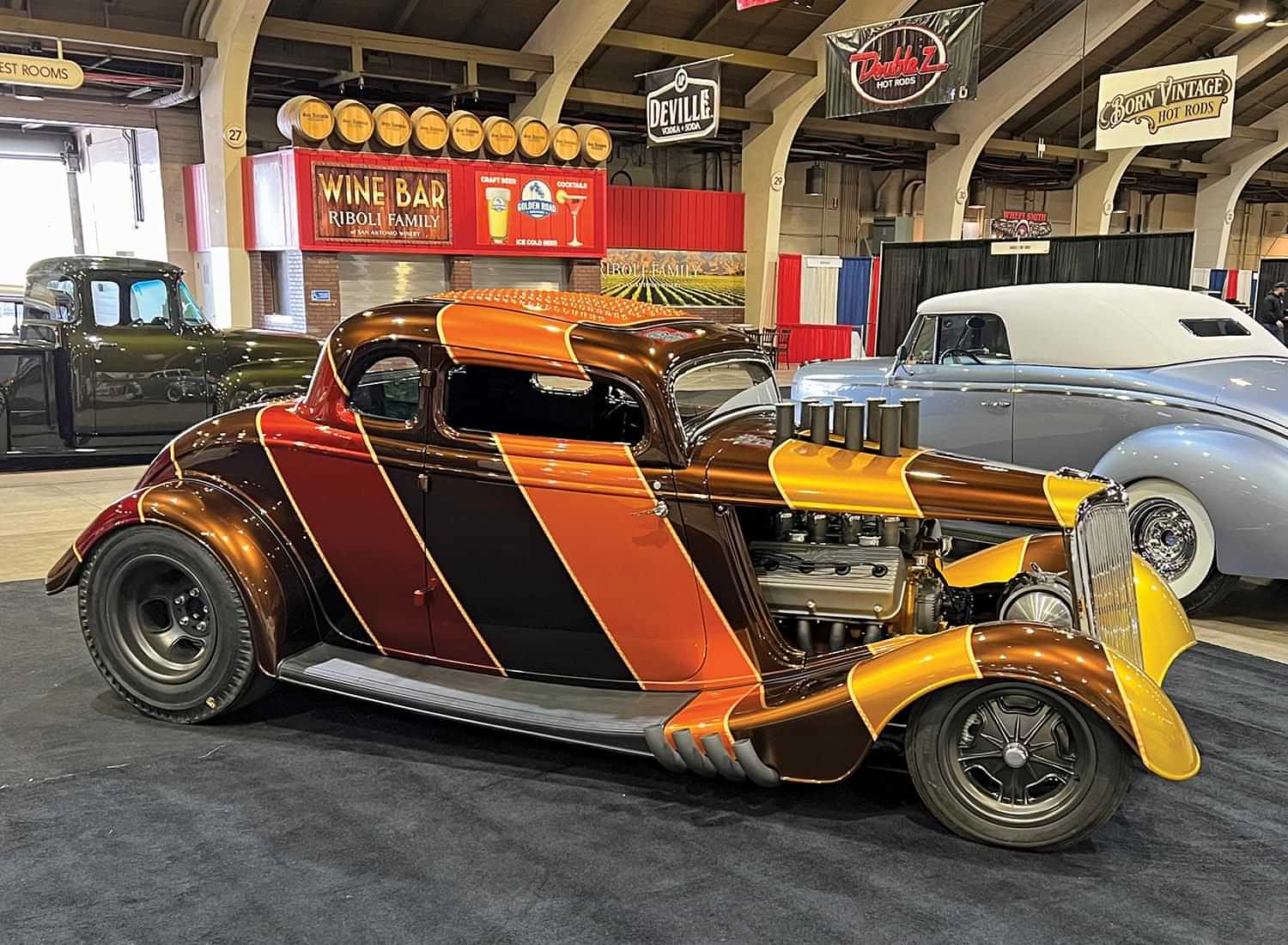 three quarter passenger side view of a ’34 Ford five-window coupe with its side hood panels removed and covered vertically with thick diagonal lines of mustard, orange, dark red and brown