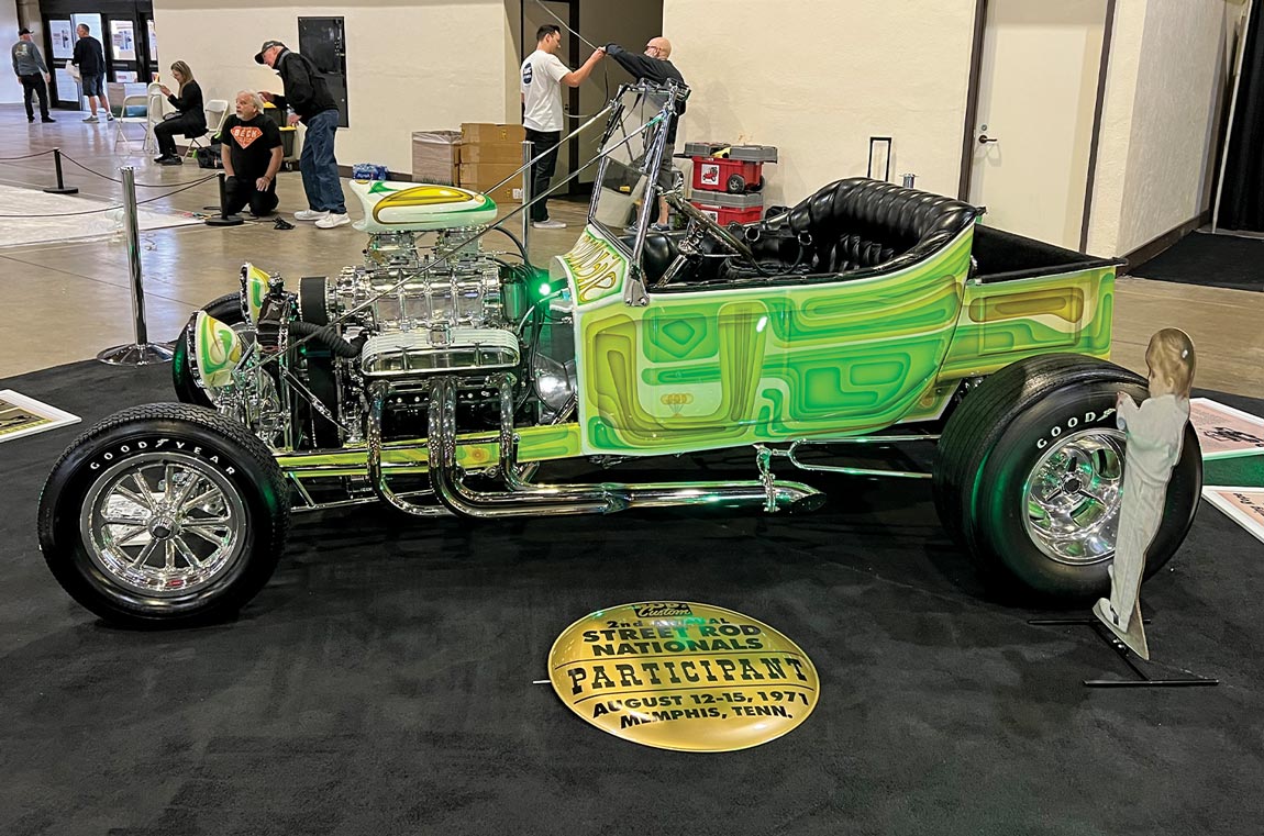 three quarter drivers side view of Terri Hollenbeck's custom painted green T-bucket with fully exposed engine and a small cardboard cutout of Terri as a toddler placed beside
