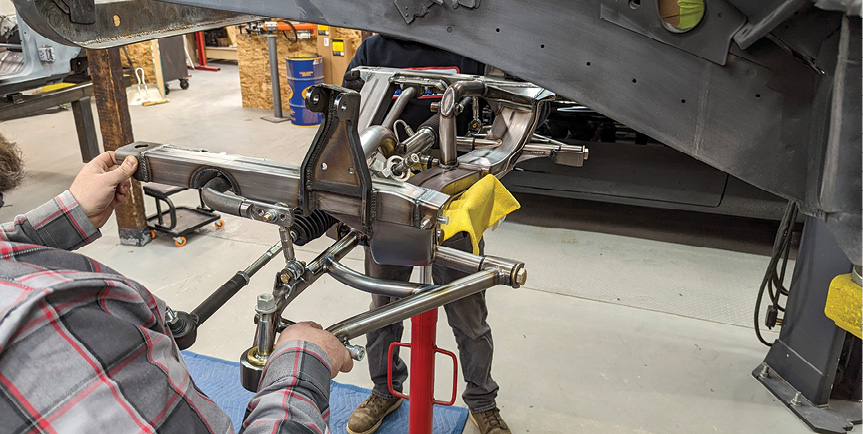 A transmission jack works well for removing the stock crossmember and installing the AME assembly. The new K-member should be installed with the steering rack, sway bar, and lower control arms bolted in place.