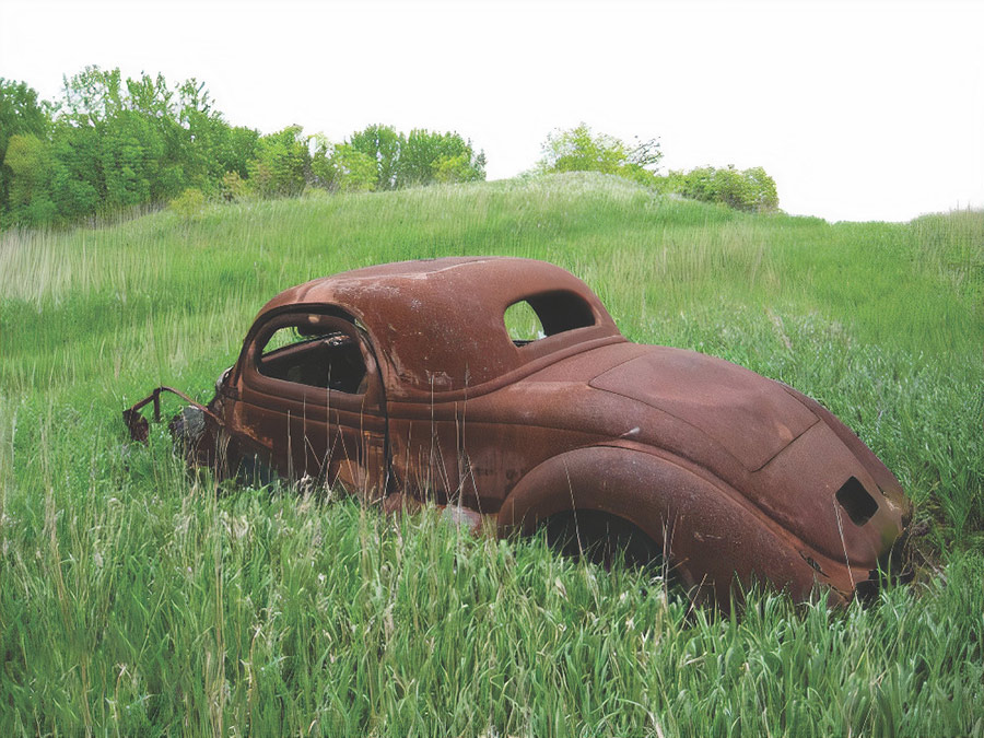 Coupe's stripped and rusted body shell in a grassy field