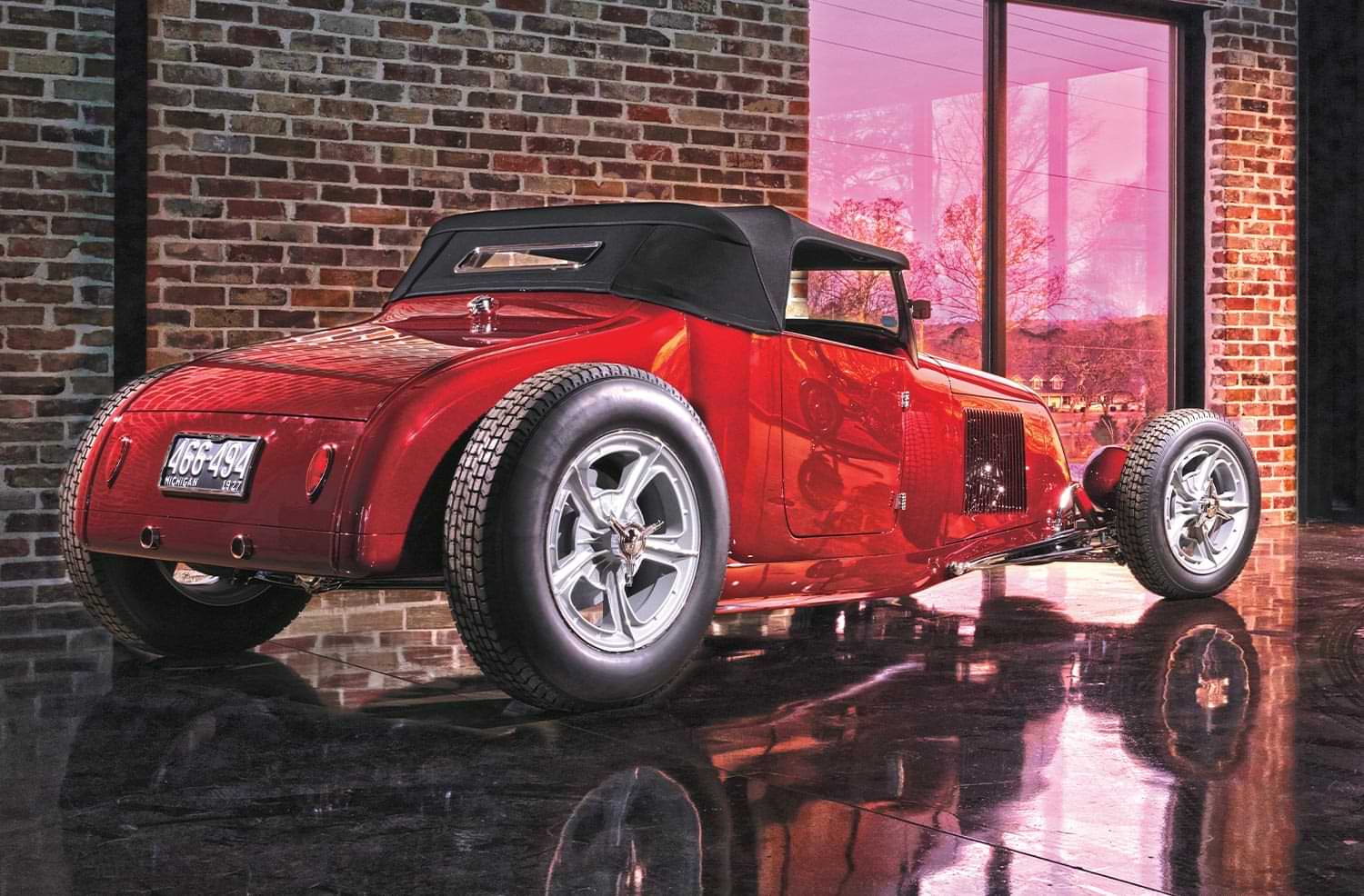 3/4ths passenger side rear view of the red '27 Ford Highboy Roadster parked beside a red brick wall