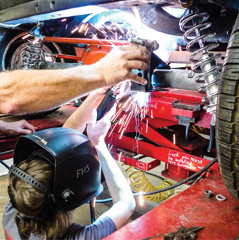 At this stage the rearend is centered, wheel alignment is satisfactory, and so is our pinion angle. Speedway’s brackets are fitting well, but we’re only tack welding for now. Lastly, let’s locate and tack weld the new Speedway Panhard bracket to the right-side axle housing. Welding and holding are Mason and Mr. Greene.