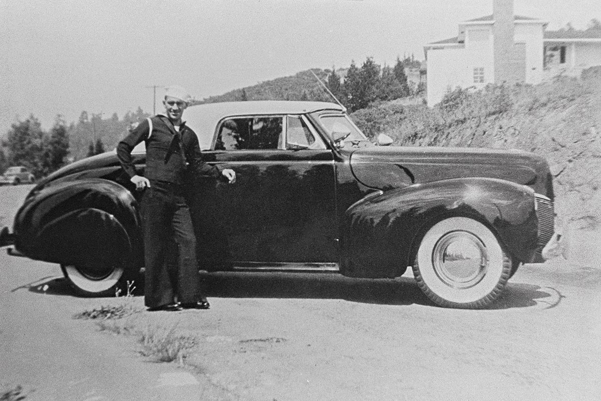 Black & white photograph of Sailor Tommy with his customized ’40 Merc convertible in San Francisco, circa 1946-47. Black and sleek, chopped Carson top, Appleton spots, seamless fenders, recessed plate chamber, and rear taillights, this car made a stunning impression on a young and aspiring custom car builder, one Joe Bailon.