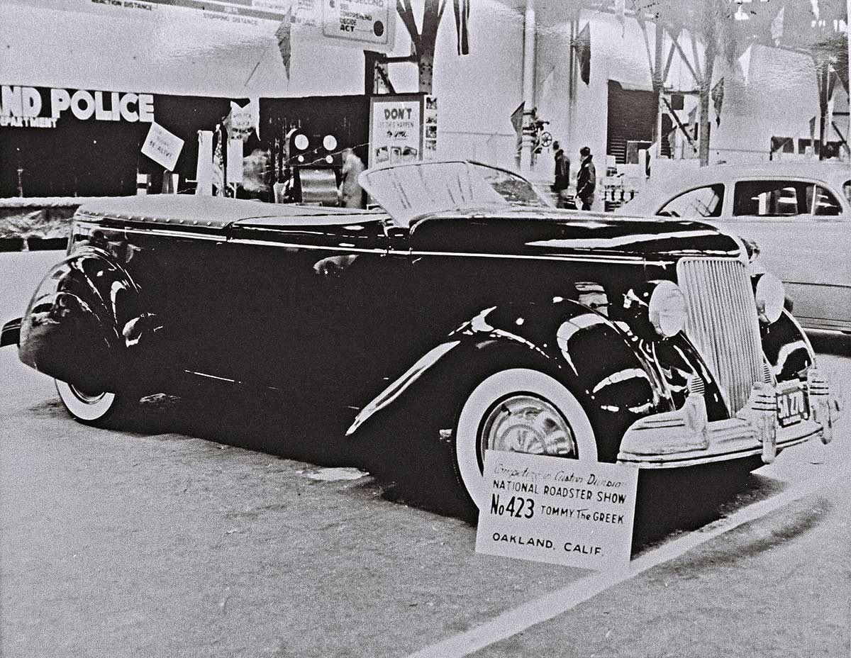 Black & white photograph of this stylishly customized ’36 Ford phaeton entered by “Tommy The Greek” in the first Oakland Roadster Show, January 1950, at the city’s Exhibition Hall. Tommy’s sensitivity to styling included seamless fenders, Duvall windscreen, removed door handles, and a low, dark silhouette.