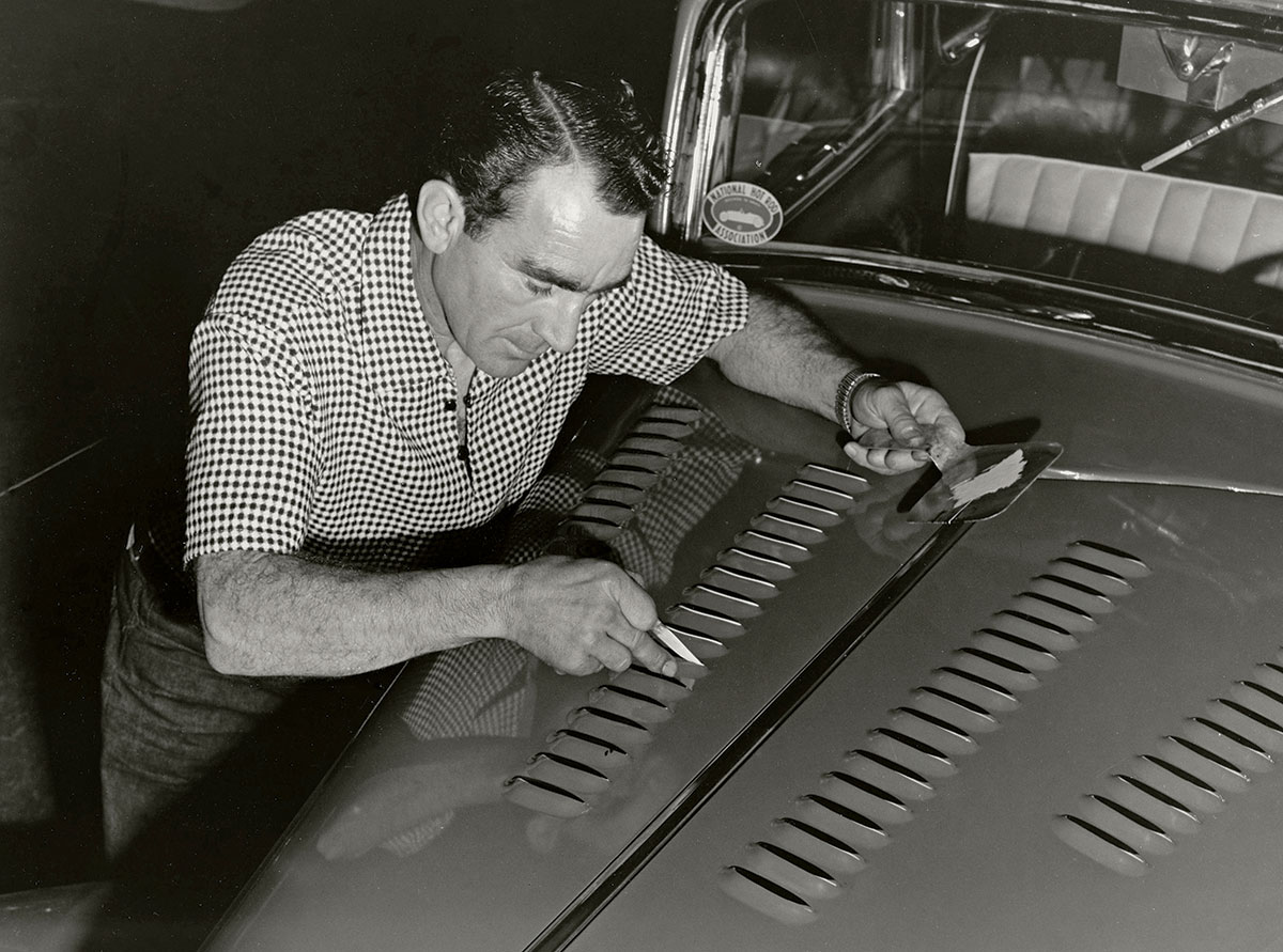 Black & white photograph of a study in concentration and perfection. Tommy precisely accents each louvre on the hood of Dean Moon’s ’34 Ford coupe. Oakland Roadster Show, 1955.
