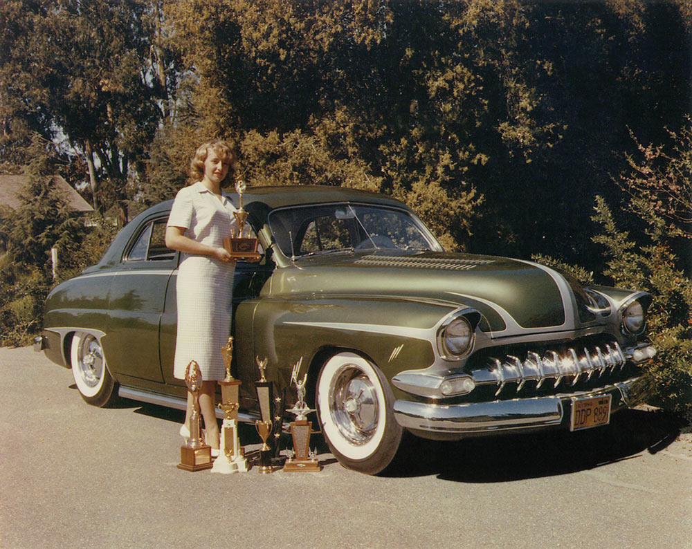 Dawn Smith with multiple trophies next to her metallic green custom '50 Mercury sedan