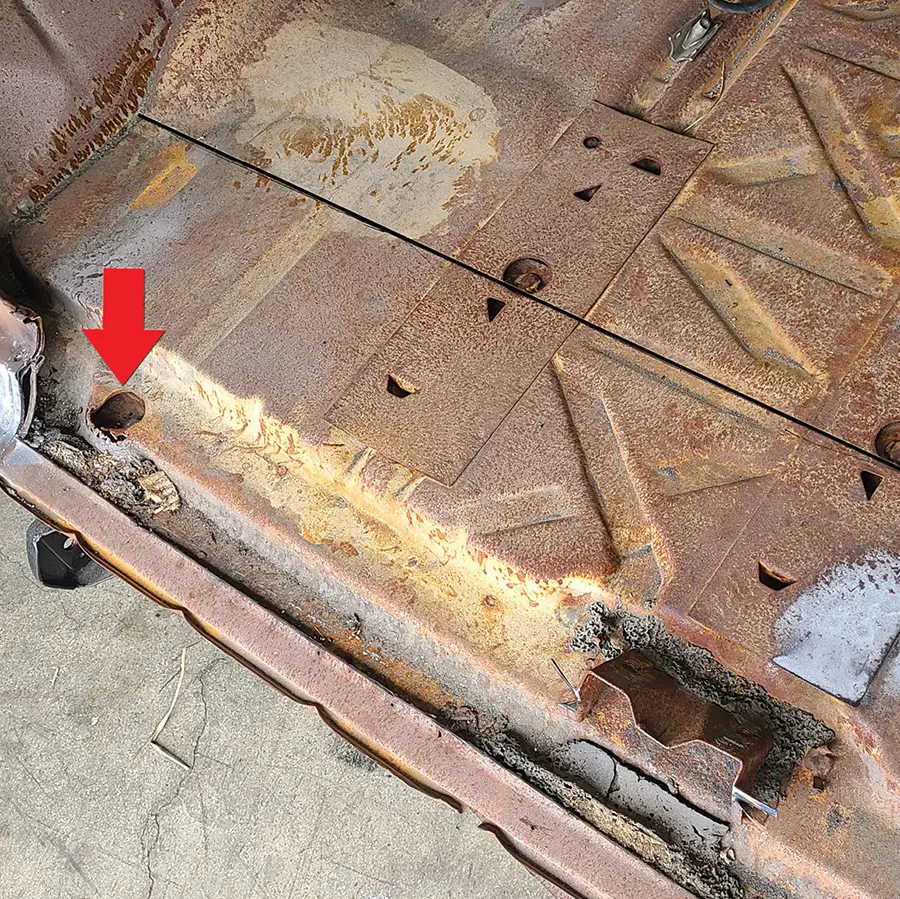 The new 10-inch-wide tailpan will lay out (see line) just to the rear of the two gas tank mounting bolts under the two spot-welded flat braces here. There are also two outboard body mount bolts (see arrow), one on each side, that will need to be removed.