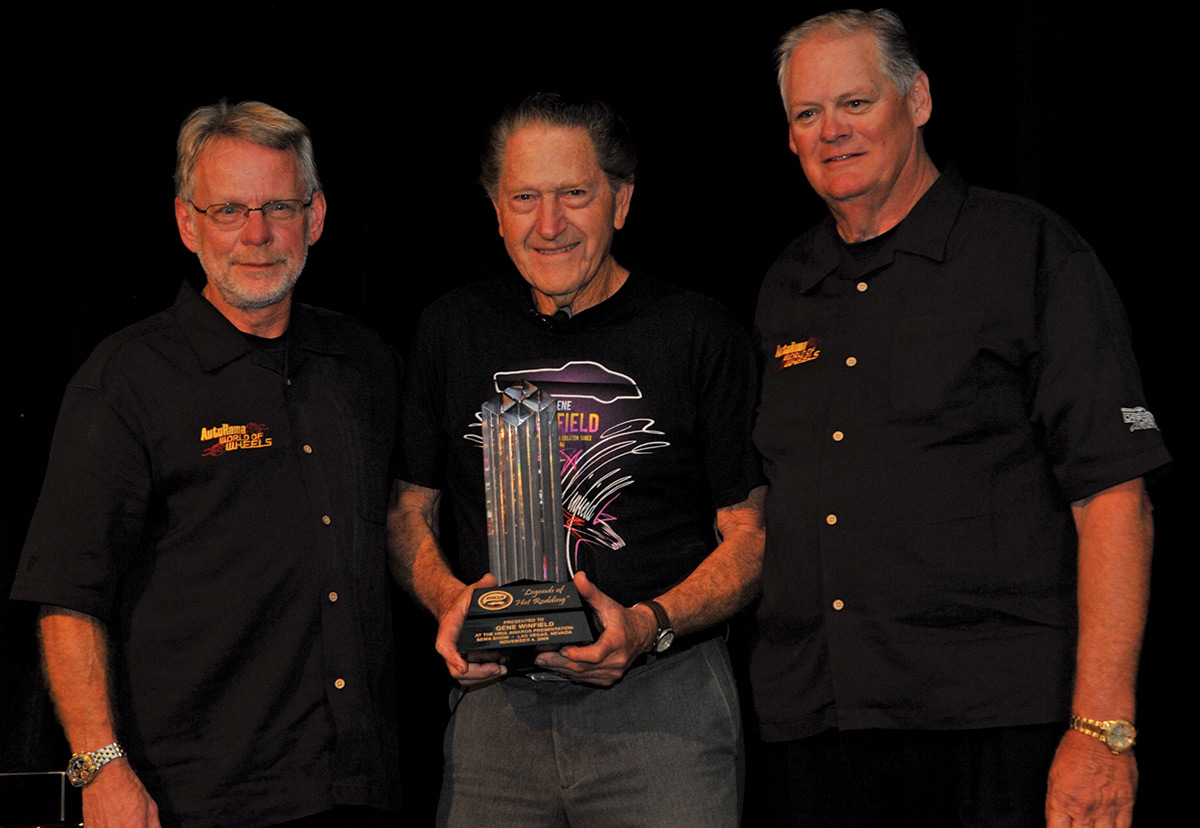 Close-up landscape photograph perspective of Gene Winfield in the middle holding his Legends of Hot Rodding award [presented by ISCA] during the HRIA dinner at the SEMA show in November 2009; Standing beside him are Flanking Gene [the late Bob Larivee Jr.](nicknamed J.R.) on the left, and Bob Millard on the right