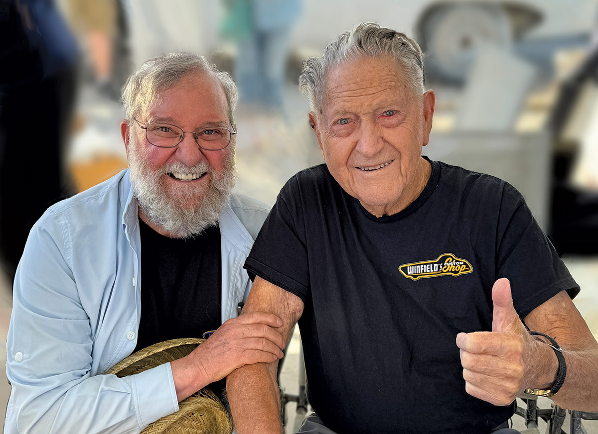 Close-up landscape photograph perspective of Modern Rodding’s own Ron Covell (to the left) posing next to Gene Winfield (to the right) as they are smiling happily excited; Ron took the time to drop by the latest in the long line of Winfield-Watson events