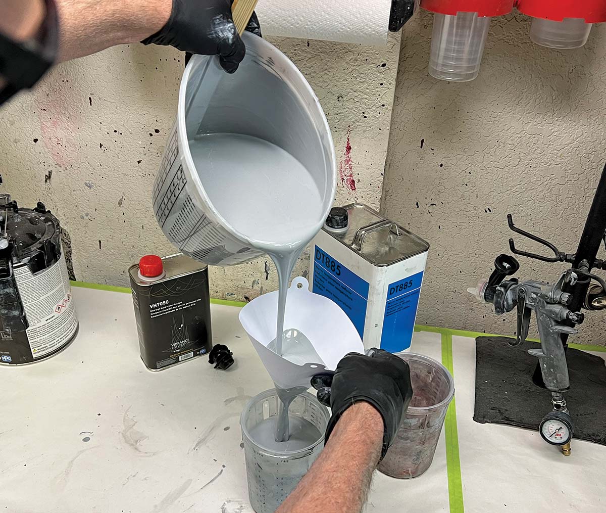 Close-up landscape photograph perspective of a person's hands pouring grey paint (primers like PPG’s high-build VP2050) into a bucket