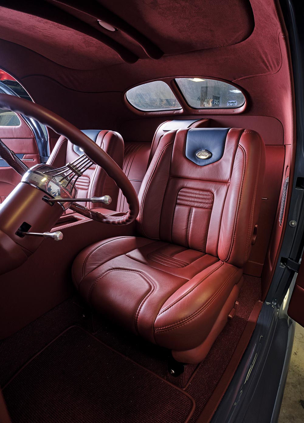 view from the open driver side door at the custom ’38 Lincoln Zephyr's red furnished interior with a focus on the driver seat