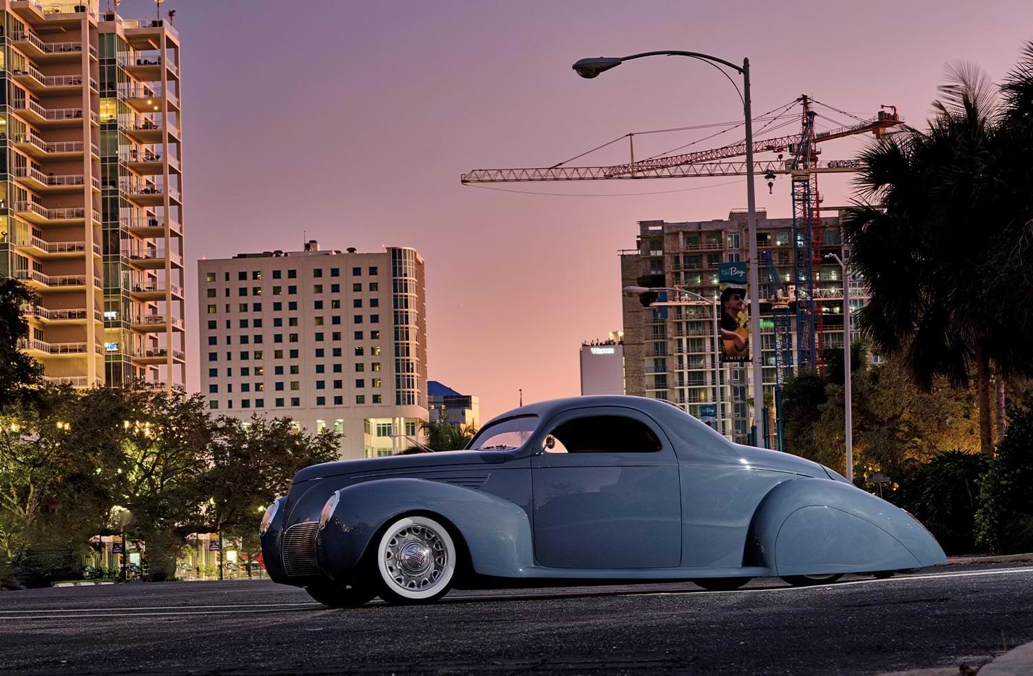 driver side profile of the custom ’38 Lincoln Zephyr parked against a city cityscape at dusk