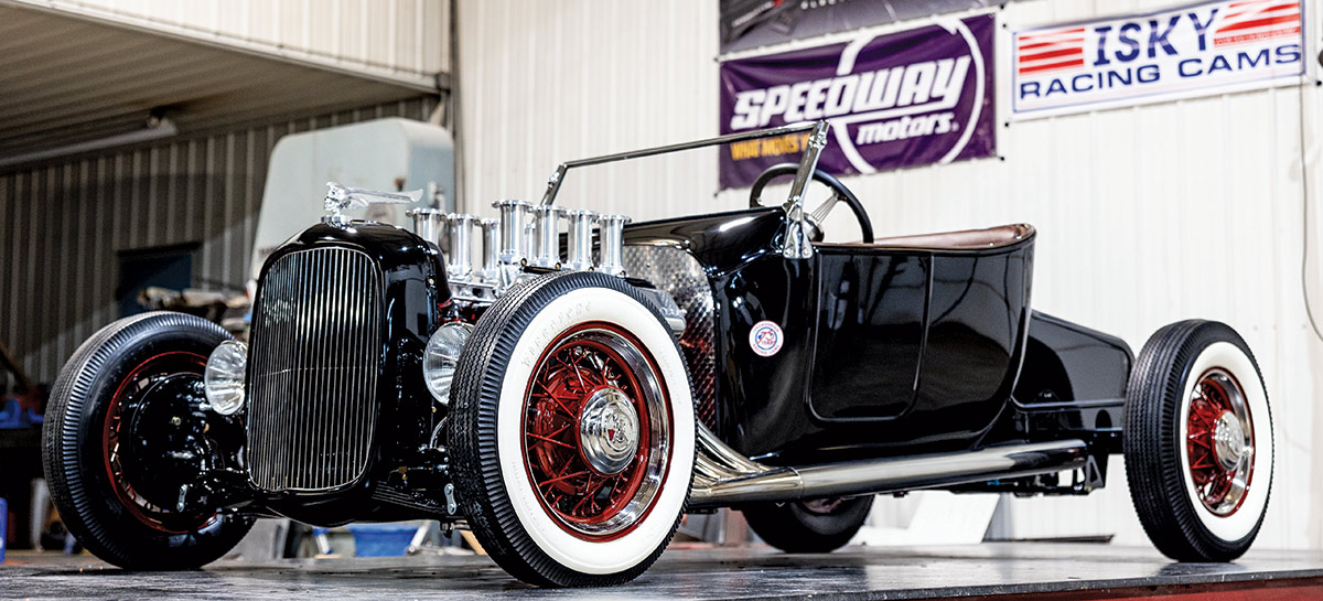 Landscape angle photograph perspective of the 1923 Isky tribute Ford roadster black car with whitewall tires on display somewhere inside a custom garage shop
