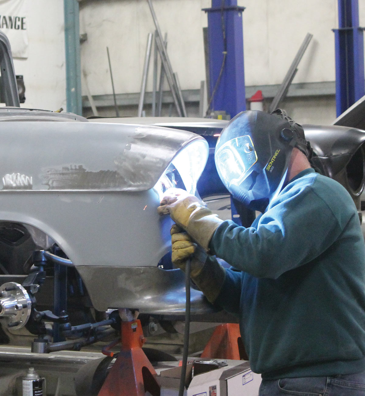 Man with welding mask and gloves, welding the panel to the headlight