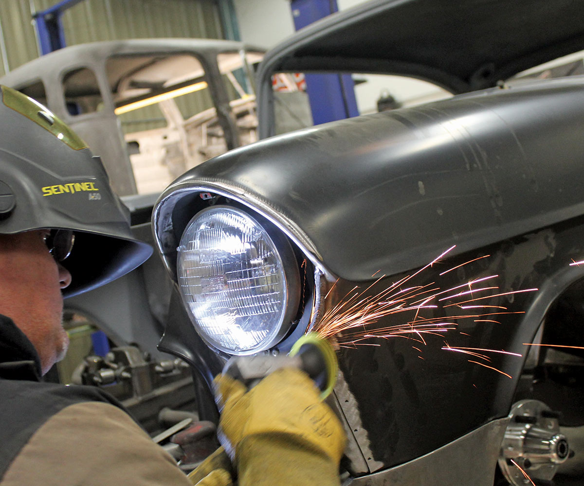 Man with yellow gloves, using a grinder to smooth out around the headlight