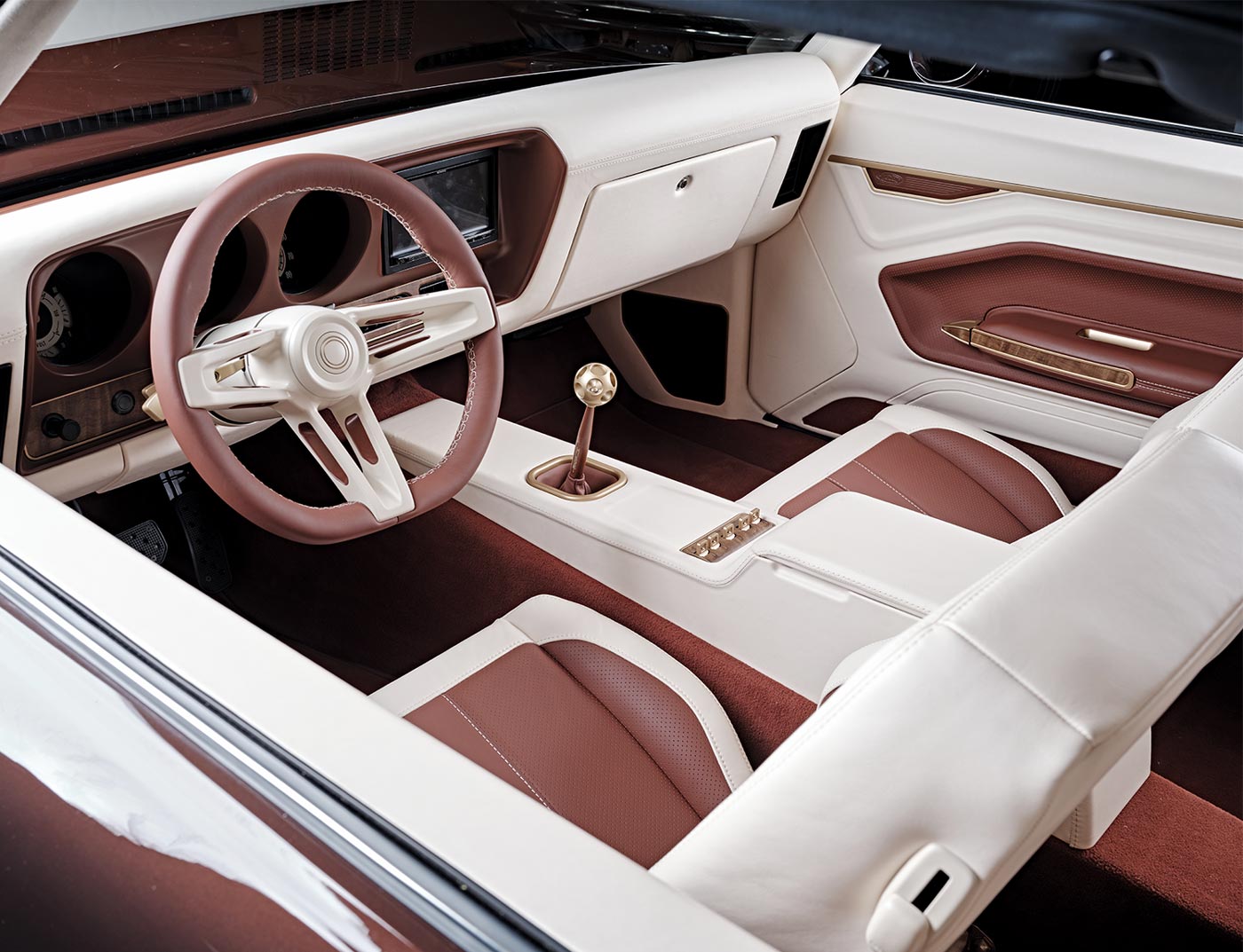 view inside the ’69 GTO driver side window with a focus on the front seating, featuring brown- and cream-colored leather stitched bucket seats