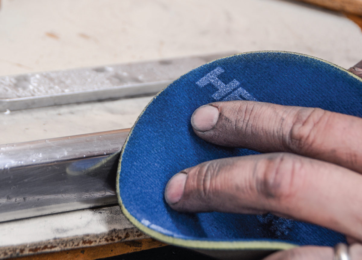 a hand holding a 3,000 grit pad continues working on the piece of trim