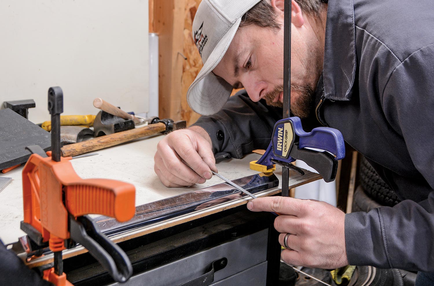 a mechanic uses simple tools on a work table, leaning in close to a piece of steel trim