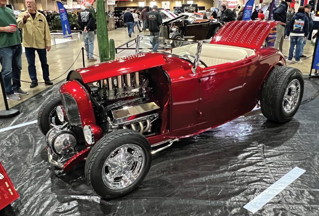 driver side view of a highly modified ruby red ’32 Ford highboy roadster with the rear gate open and the engine side panels removed