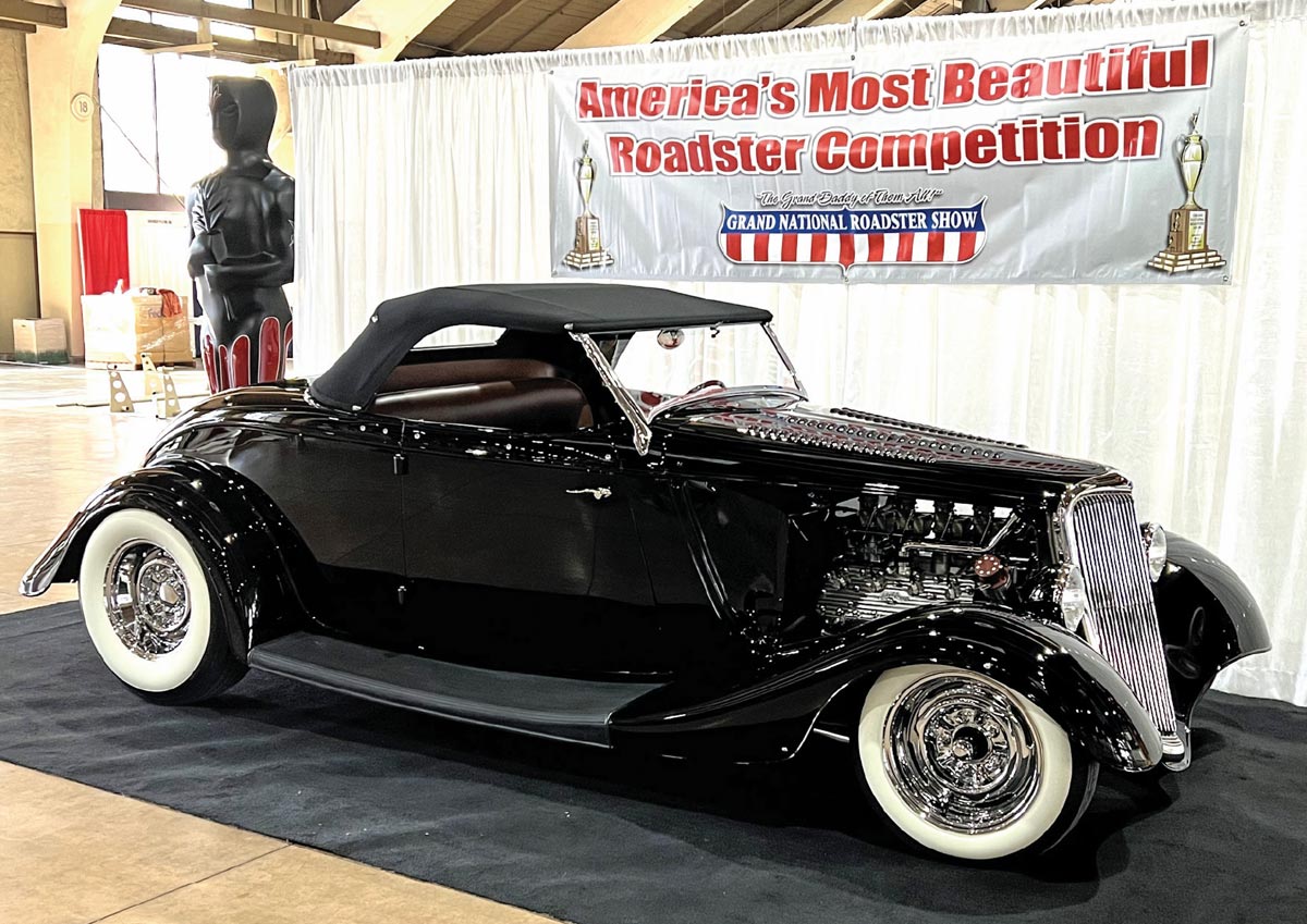 passenger side of a black Flathead-powered ’34 Ford roadster with a black top and white wall tires