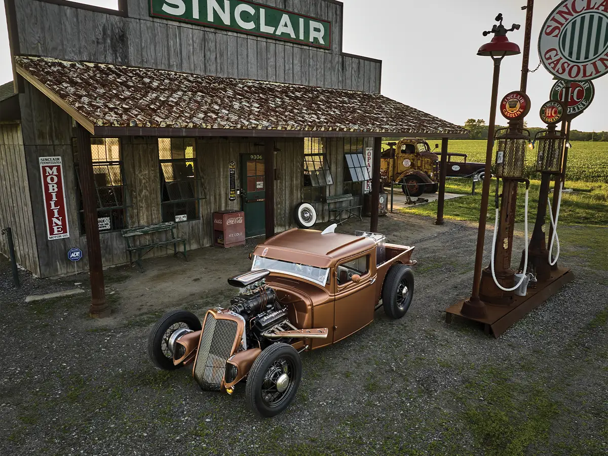wide high angle shot of the custom copper ’34 Ford pickup parked in front of an old-style Sinclair gas station