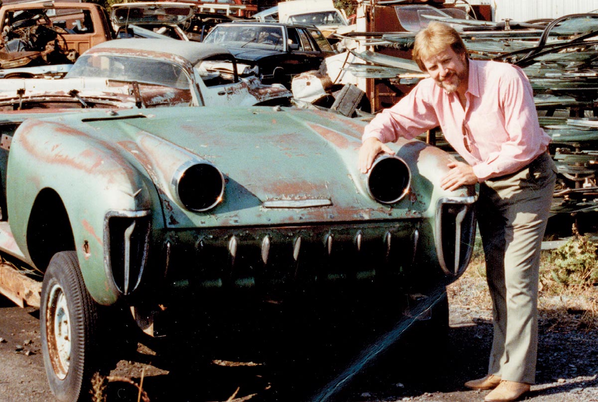 Landscape outdoor vintage close-up photograph view of Joe Bortz, a real hod rodder, smiling with the GM Motorama concept car, the ’55 Chevy Biscayne, cut in half and ready for the crusher when he found and rescued it in the scrapyard area; One of six concept cars called the “… Picassos and Rembrandts of this automotive generation …” was painstakingly restored.