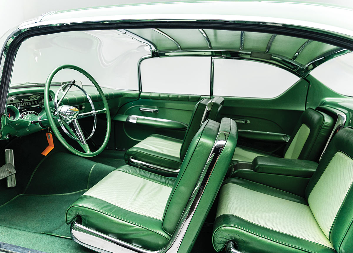 Landscape close-up side interior photograph view of a light mint green colored ’55 Chevy Biscayne showcasing the driver's seat, three other passenger seats, steering wheel, dashboard area, gas pedal, brake pedal, and two other closed doors